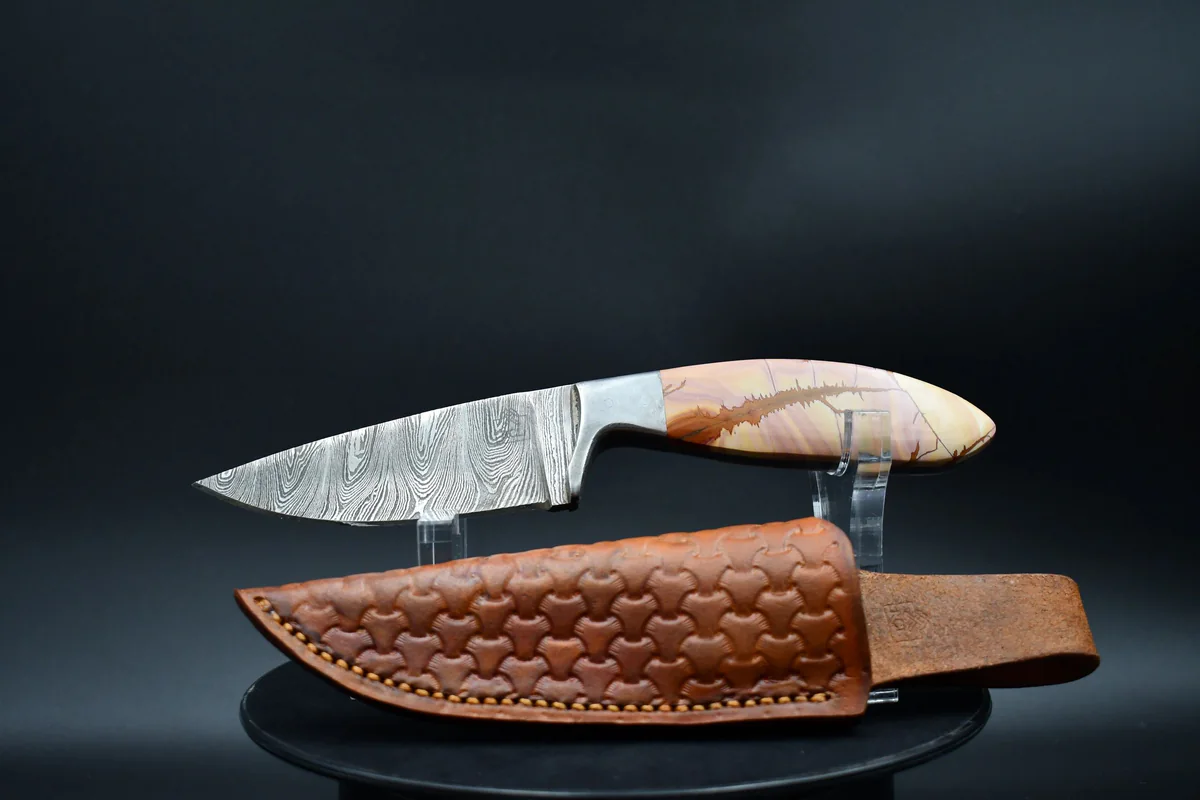 Completed custom fixed-blade knife with a patterned blade and leather sheath
