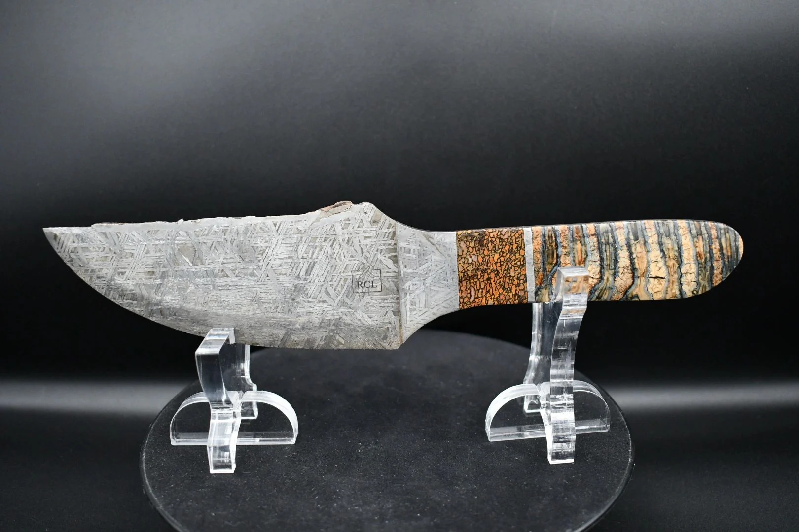 Custom patterned fixed-blade knife with a striped natural-material handle on a clear display stand